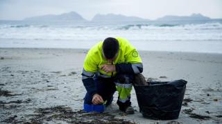 Un hombre recoge los pellets de plástico acumulados en la playa de Patos, en Nigrán, A Coruña.