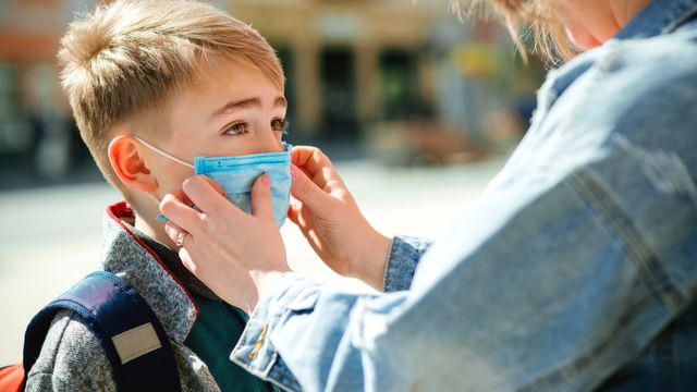 Madre pone una mascarilla a su hijo, en una imagen de Shutterstock.