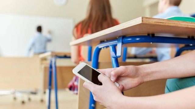 Un alumno en clase utiliza el móvil.