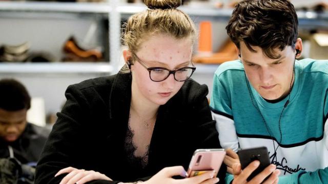 Dos adolescentes usan sus dispositivos en el aula.