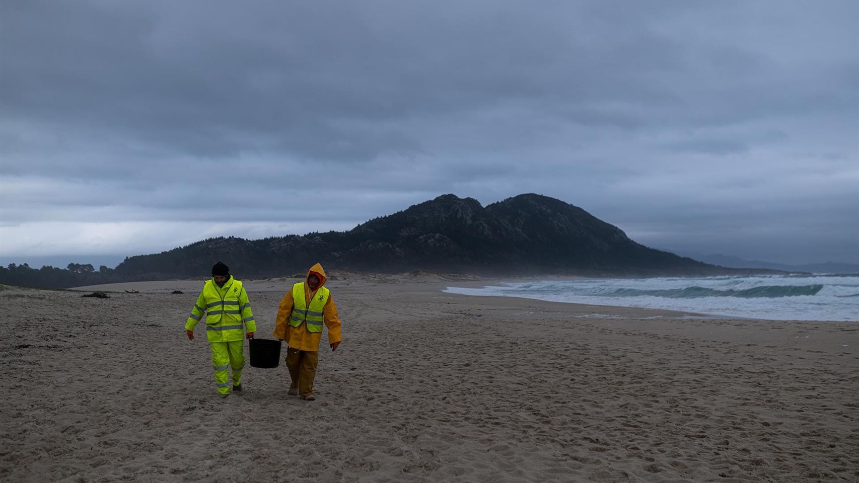 Dos hombres cargan un cubo lleno de pélets, en la playa Area Maior.