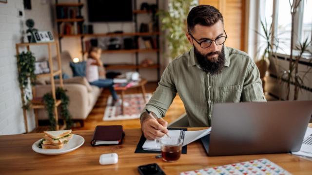 Padre trabajando desde casa; de fondo, su hija.