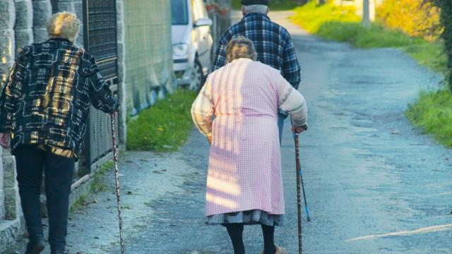 Tres personas mayores caminan por un pueblo.