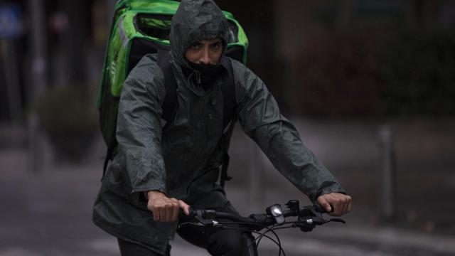 Un 'rider' (repartidor) trabaja bajo la lluvia protegido con un impermeable