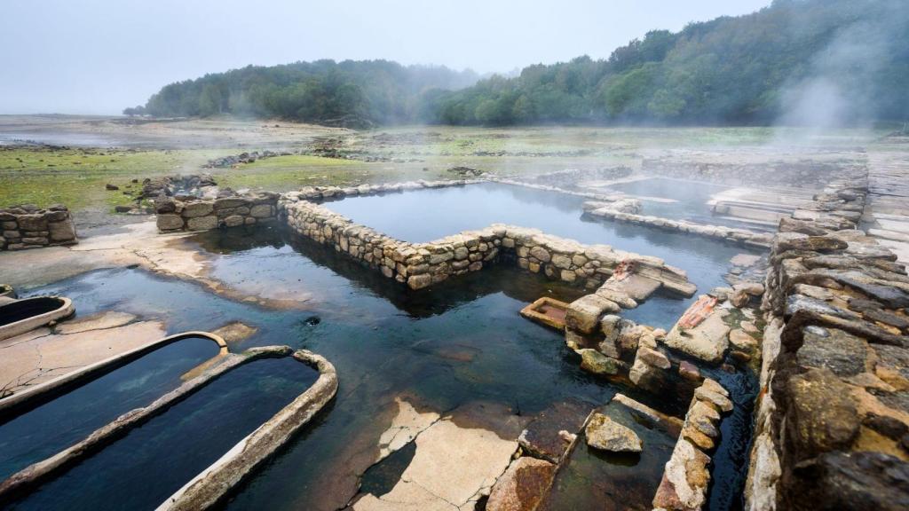 Natural Roman baths outdoors with hot steam and thermal water. Old roman hot springs open air spa and hot natural thermal water in small pools and stone bathtubs. Aquis Querquennis Bande Galicia Spain