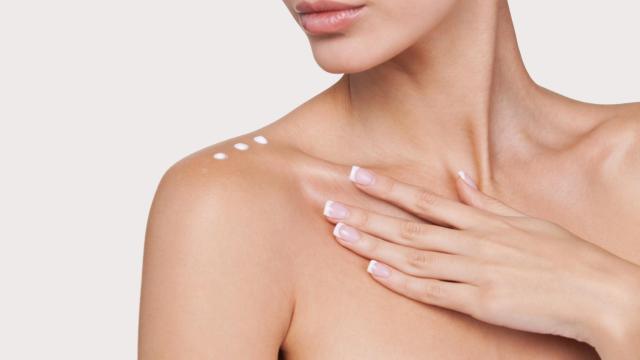 Una mujer aplicándose crema en el escote.