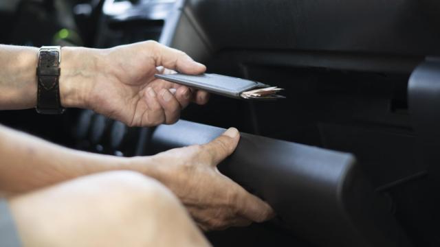 Imagen de una persona guardando los papeles en la guantera del coche.