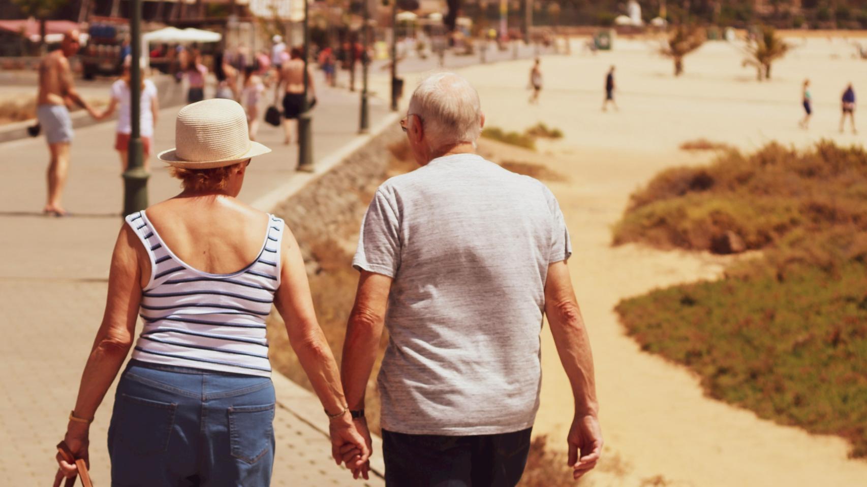 Una pareja de jubilados camina por un paseo marítimo.