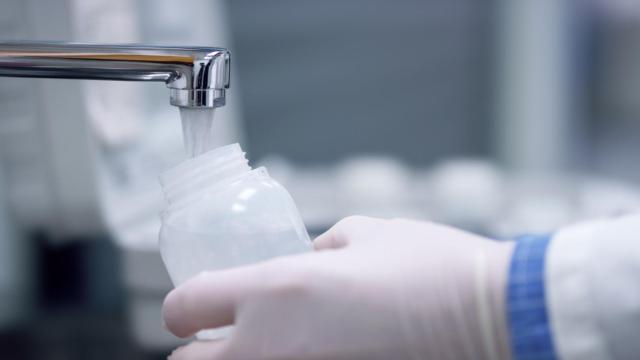 Imagen de archivo científico rellenando un recipiente con agua de grifo.
