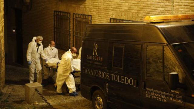 Los servicios funerarios sacan de la vivienda a uno de los fallecidos.