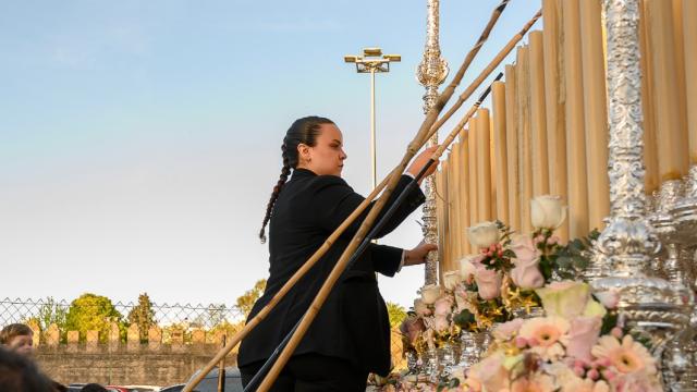 Una miembro del equipo de 'Servicios Cofrades' ayuda en el encendido de la candelería de un palio.