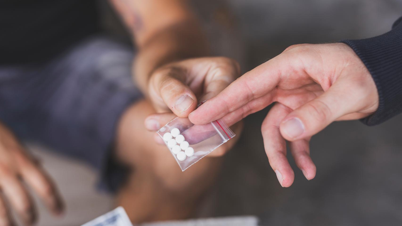 Un hombre proporciona a otro una bolsita con pastillas, en una imagen de Shutterstock,