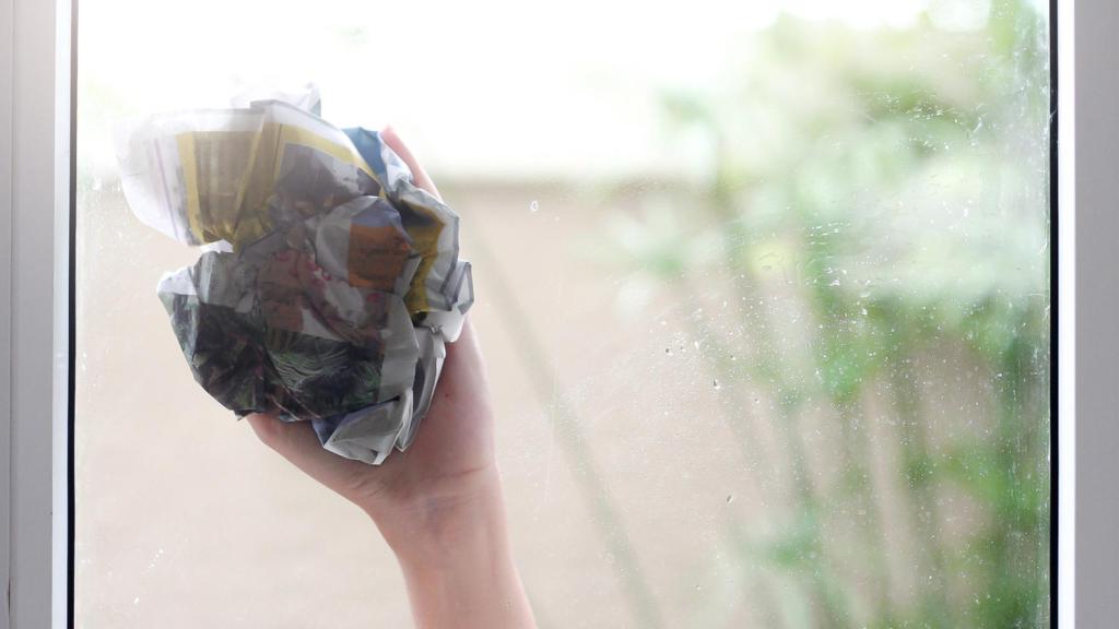 Imagen de una persona limpiando un cristal con papel de periódico