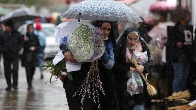 Mujeres iraníes caminan bajo la lluvia en un mercado de flores en Teherán.