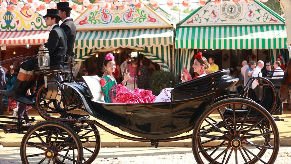 Dos mujeres vestidas de flamenca pasean en un coche de caballos.