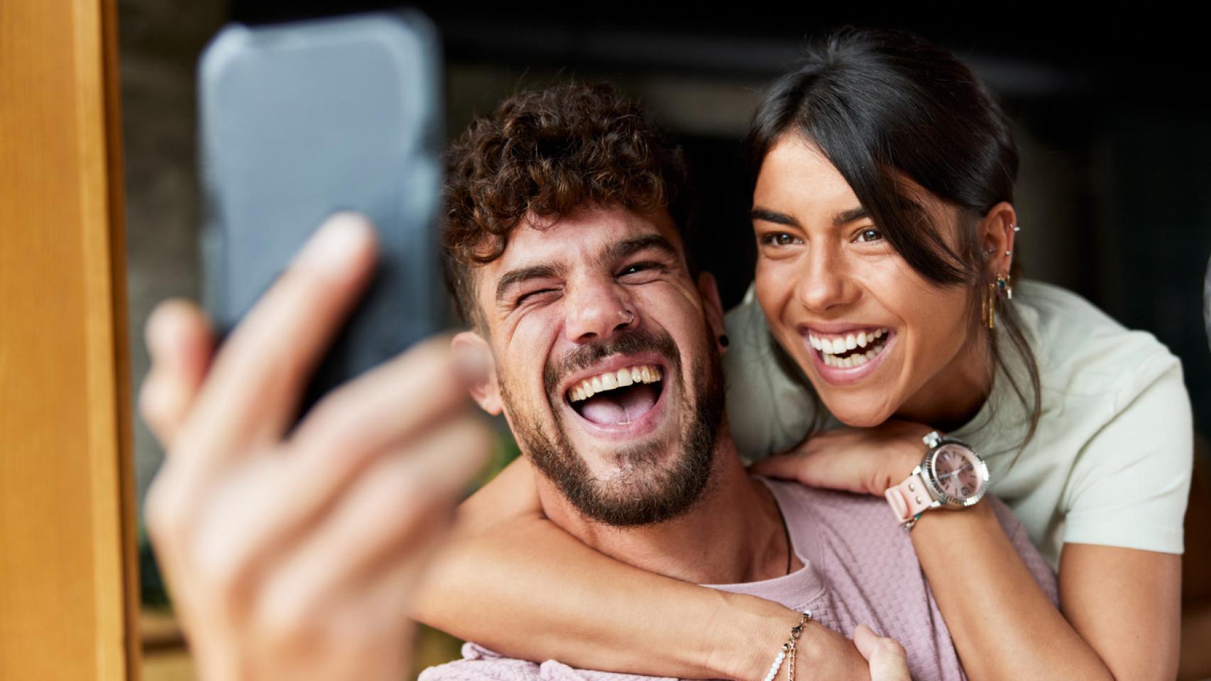 Pareja sonriendo mientras se hacen un selfie.