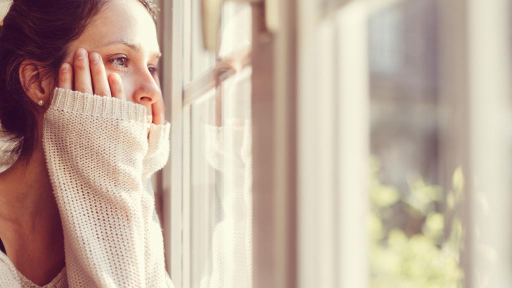 Mujer mirando por la ventana apenada.