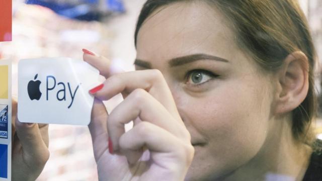 Una trabajadora pega el logo de Apple Pay en el escaparate de una tienda.