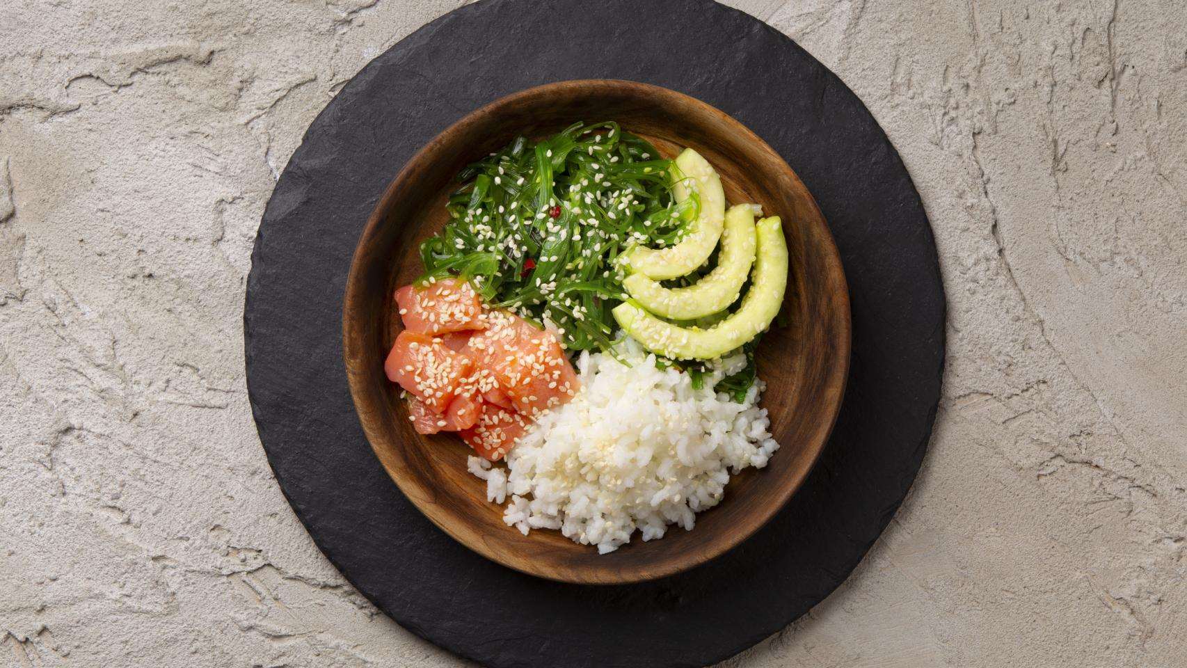 Primer plano de un plato con salmón, algas, aguacate y arroz.