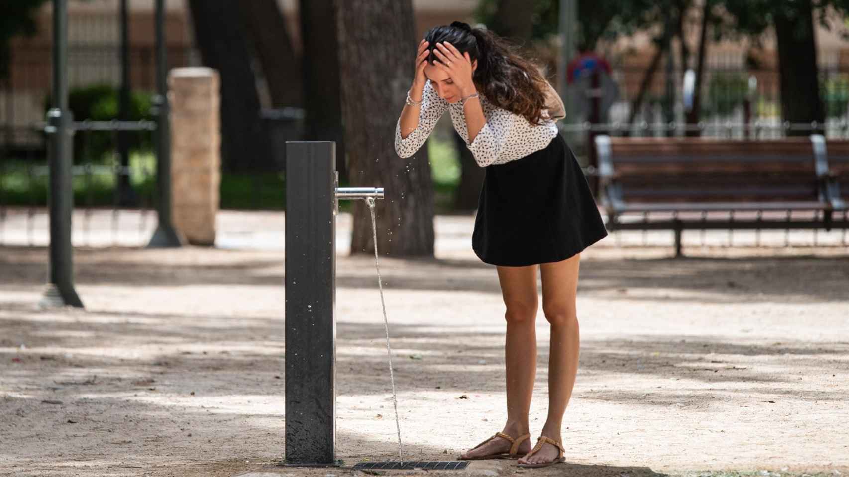 Una chica refrescándose en una fuente.