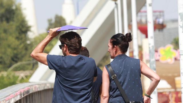 Dos personas cruzan el Puente de la Barqueta bajo las altas temperaturas sevillanas.