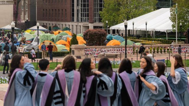 Varias estudiantes de Columbia con toga posan delante del campamento en apoyo a Gaza.
