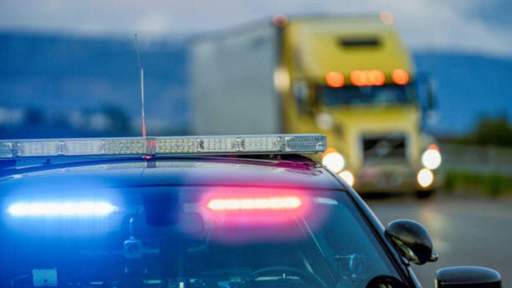 Un coche de Policía con señales luminosas al paso de un camión