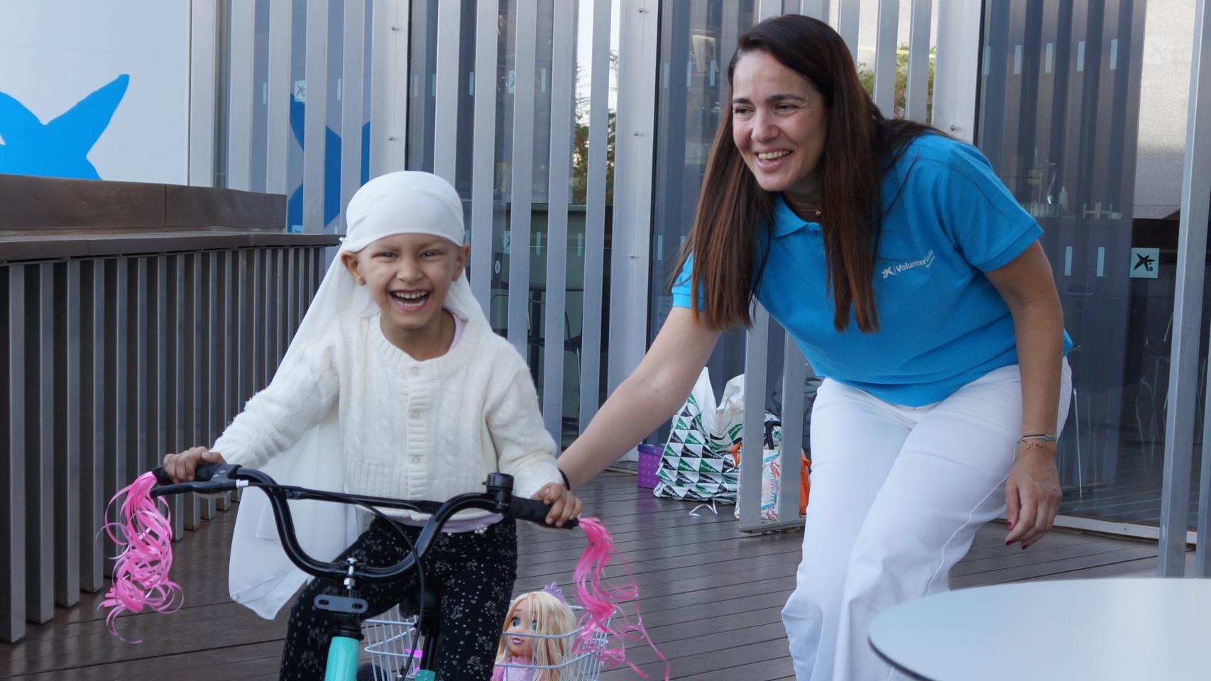 Imagen de una niña disfrutando de su bicicleta con una voluntaria de la Fundación Pequeño Deseo.