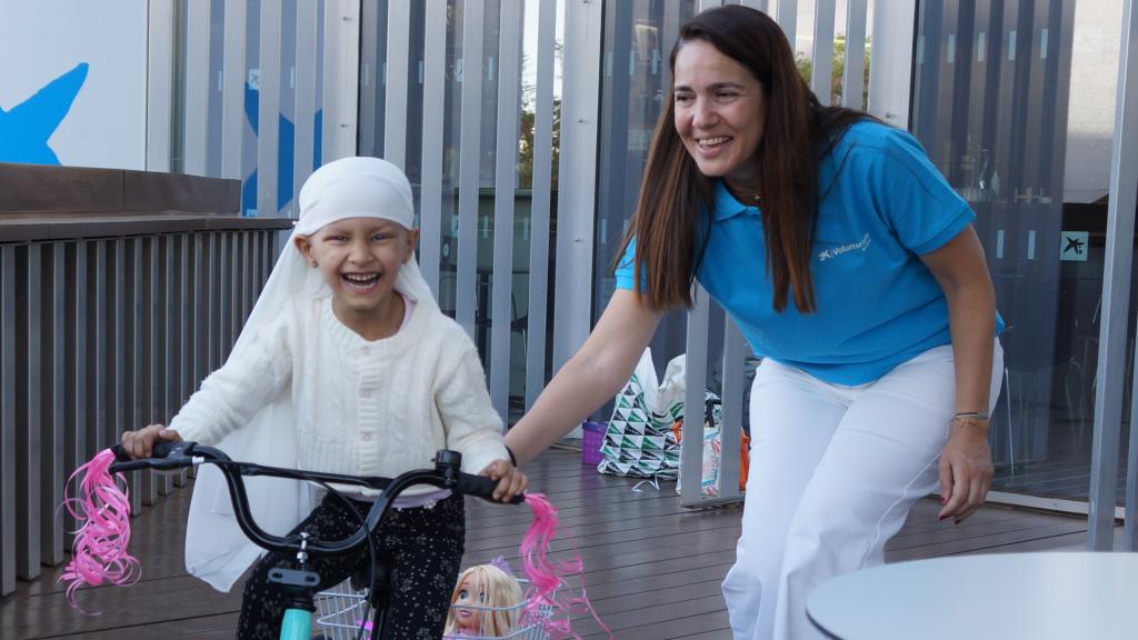 Imagen de una niña disfrutando de su bicicleta con una voluntaria de la Fundación Pequeño Deseo.