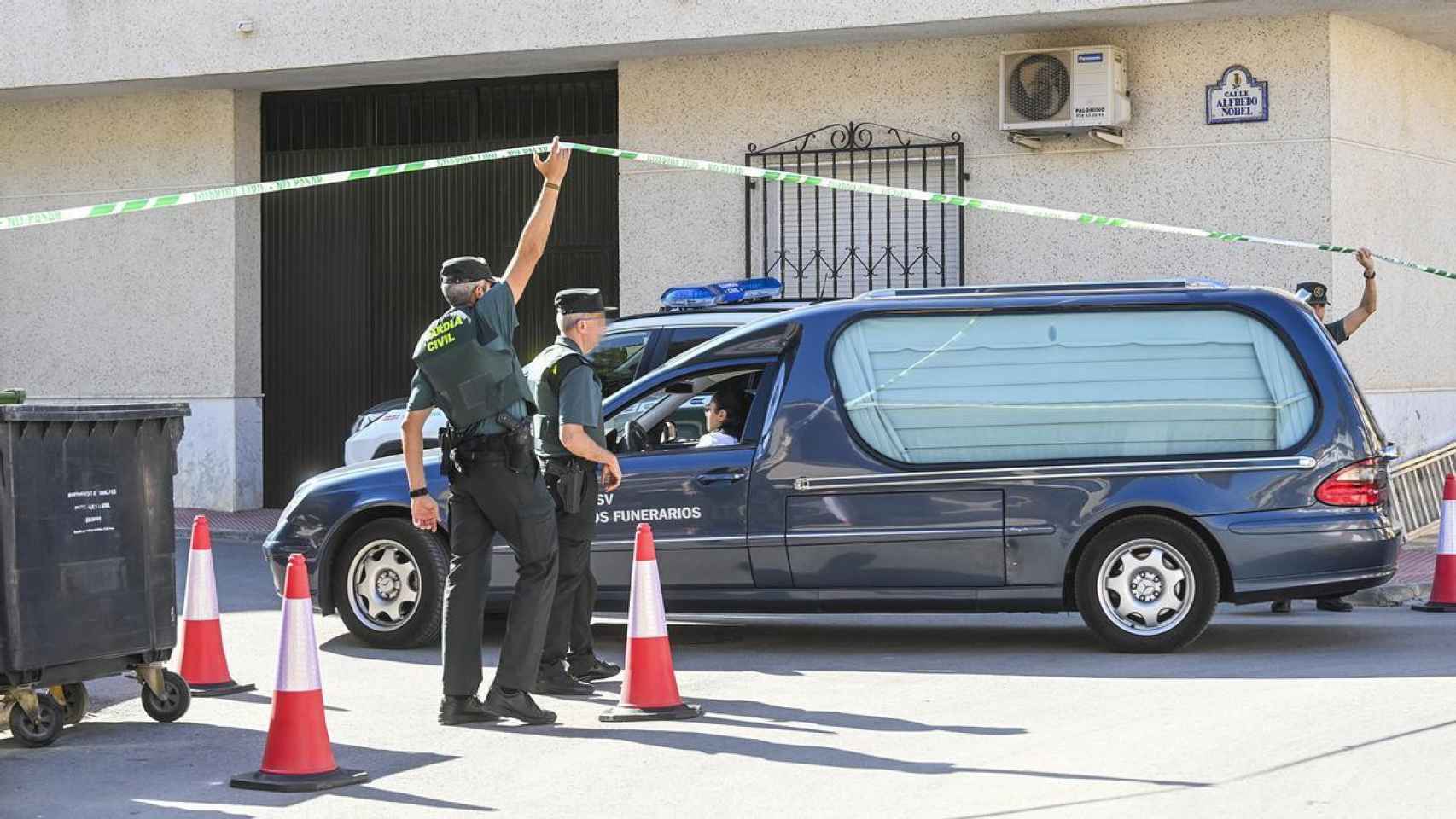 Tres agentes de la Guardia Civil facilitan el paso de un coche fúnebre a la Calle Alfredo Nobel.