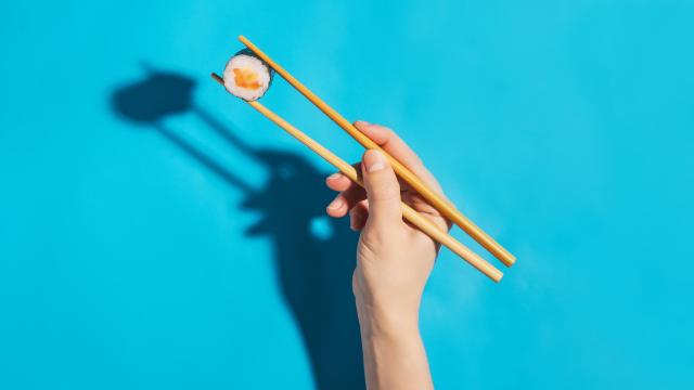 Una mano sostiene un maki con unos palillos.