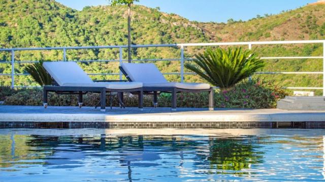 Dos tumbonas en el borde de una piscina rodeada de naturaleza.