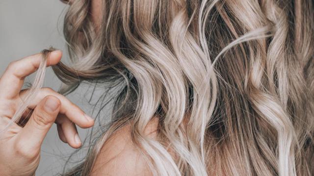 Mujer con un mechón de su cabello rizado en la mano.