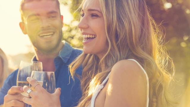 Pareja riéndose con una copa de vino en la mano.