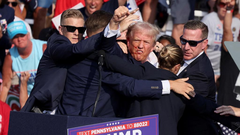 El candidato presidencial republicano y expresidente estadounidense, Donald Trump, hace un gesto con el rostro ensangrentado mientras es asistido por personal del Servicio Secreto de Estados Unidos, después de que le dispararan en la oreja derecha durante un mitin de campaña en el Butler Farm Show en Butler, Pensilvania.