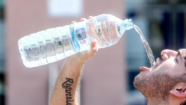 Un joven bebe agua de una botella para refrescarse.