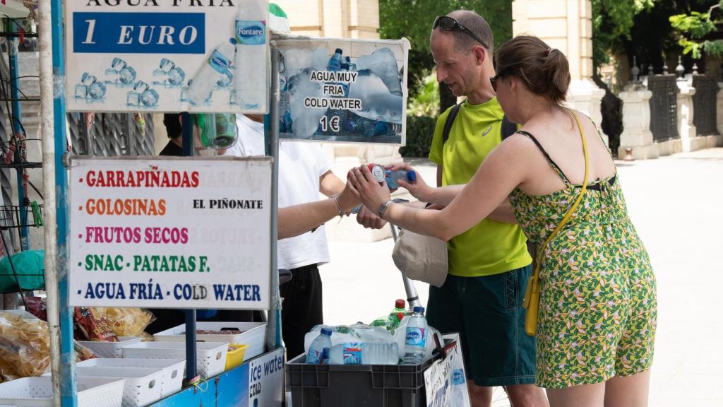 Unos turistas compran agua en un puesto callejero de Sevilla.