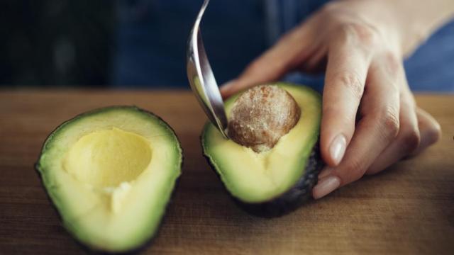 Mujer quitando la semilla del aguacate con una cuchara.