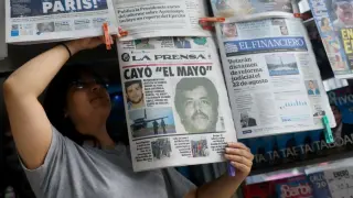 Una mujer coloca en un kiosko de la Ciudad de México un periódico que lleva en portada la detención de 'El Mayo'.