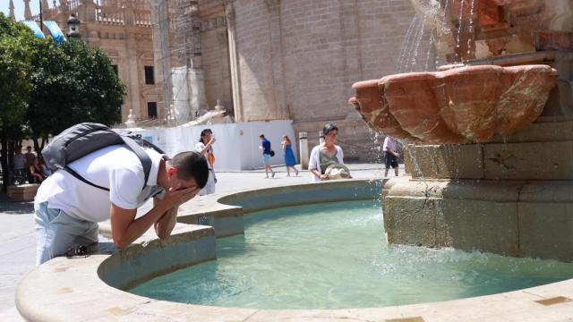 Un joven se refresca en la fuente de la Plaza Virgen de los Reyes para soportar el calor de Sevilla.