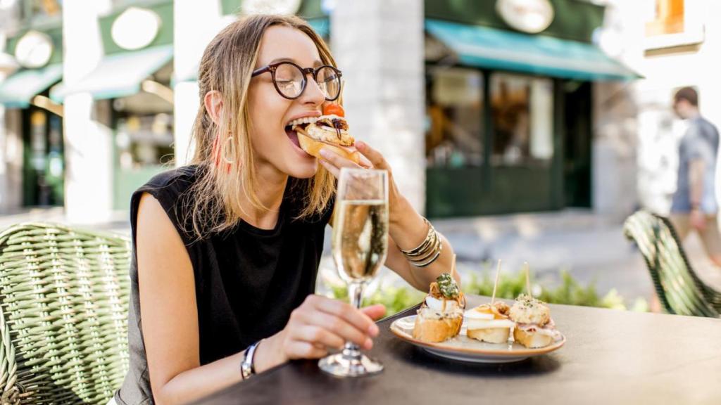 Una mujer comiendo pinchos y tapas en una terraza.