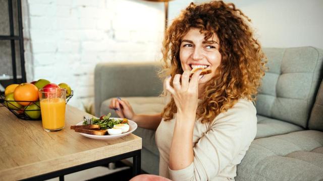 Mujer comiendo en el salón de su casa.