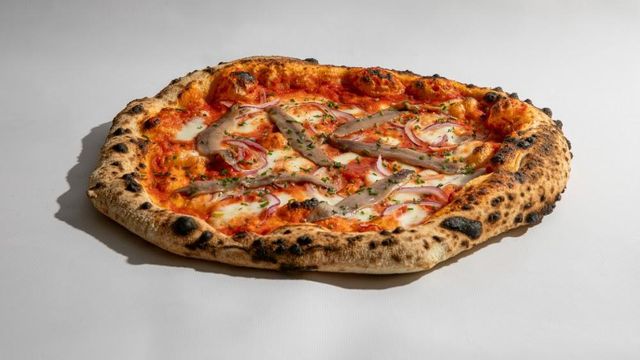 Pizza de mozzarella, cebollino y cebolla roja coronada con filetes de anchoa.