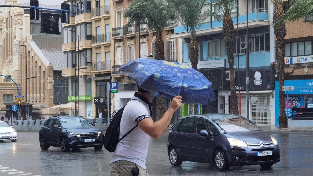Un peatón cruzando Alfonso el Sabio bajo la lluvia en Alicante.