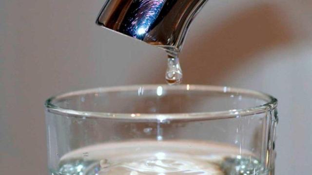 Un vaso con agua bajo un grifo que gotea.