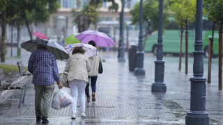 Varias personas caminan bajo la lluvia.