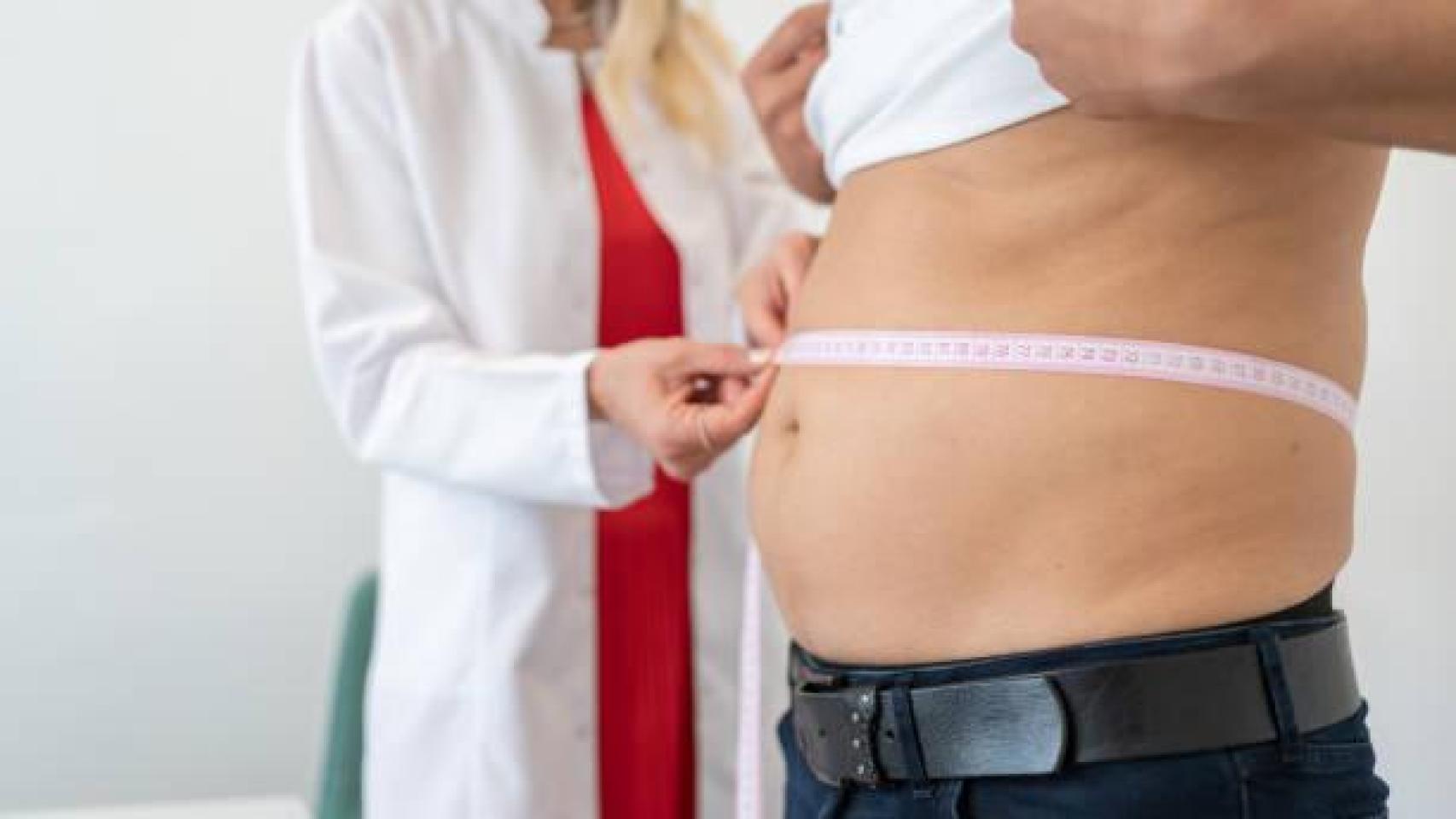 Una médico mide el abdomen de un hombre con un poco de sobrepeso.