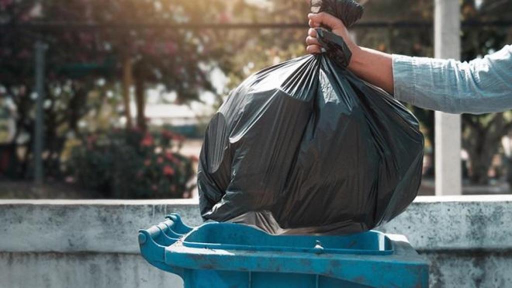 Una persona tirando la basura en un contenedor