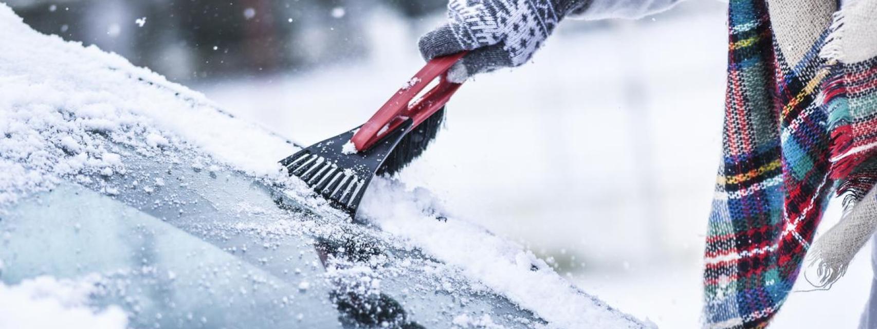 Una persona quitando el hielo del parabrisas de su coche.