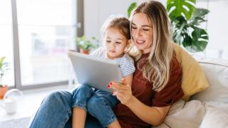 Madre con su hija en brazos mirando una tablet.
